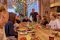 Bayern-Botschafter und Slowfood-Gastronom Uli Brandl in seinem Restaurant „’s Handwerk“ Freunde sitzen gemeinsam in einem Restaurant um einen Tisch. Am Tischende steht der Restaurantbesitzer Uli Brandl.