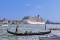 Eine venezianische Gondel fährt auf einem breiten Strom. Im Hintergrund liegt ein großes Kreuzfahrtschiff an.