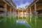 Blick in ein altes Römisches Bad in Bath. Im grünblauen Wasser spiegelt sich das beeindruckende Gebäude.