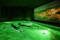 Zwei Menschen liegen entspannt in einem grün beleuchteten Becken. Um sie herum ist es dunkel. An einer Seite ist das Bild einer im dunkeln erleuchteten Stadt zu sehen.