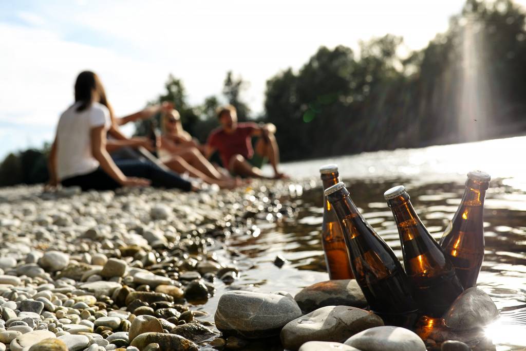 Flaschen stehen zum Abkühlen in der Donau, im Hintergrund sitzt eine Gruppe junger Menschen zusammen.