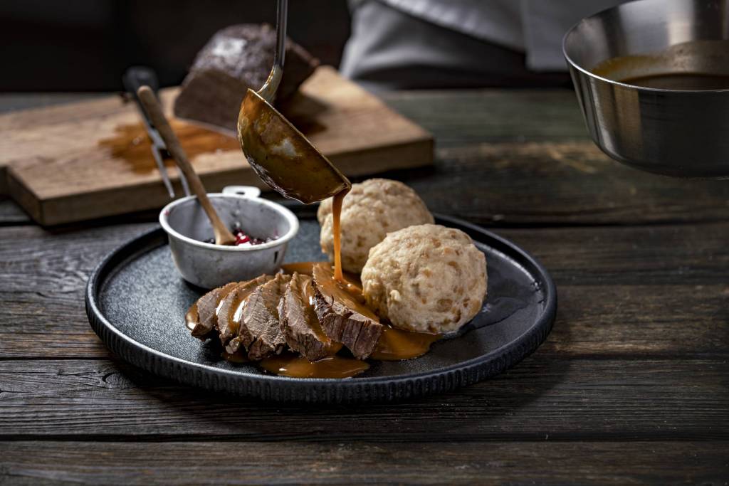 Hirschbraten mit Knödel auf dunklem Teller