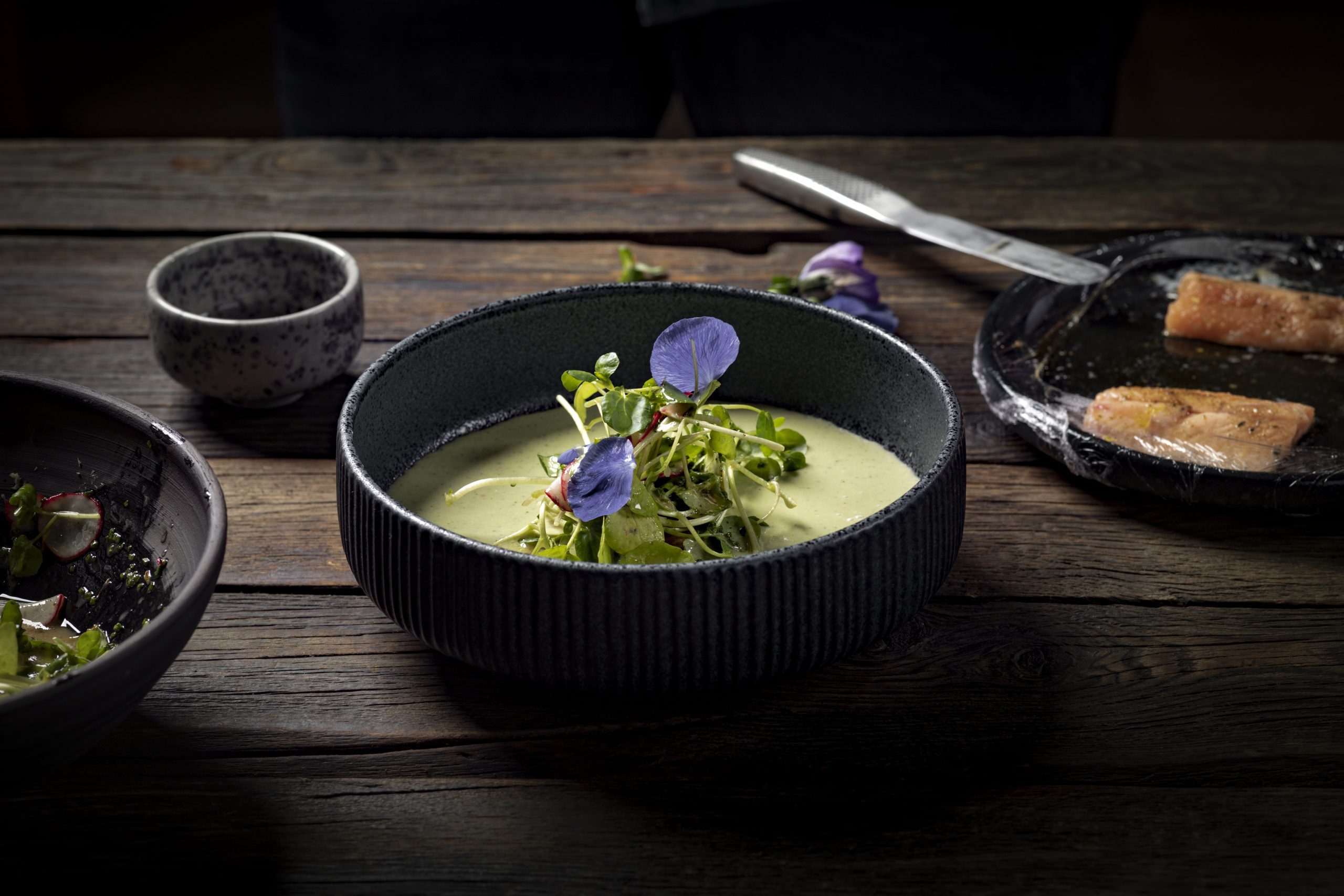 Kr&auml;utersuppe mit pochiertem Saibling serviert auf dunklem Teller