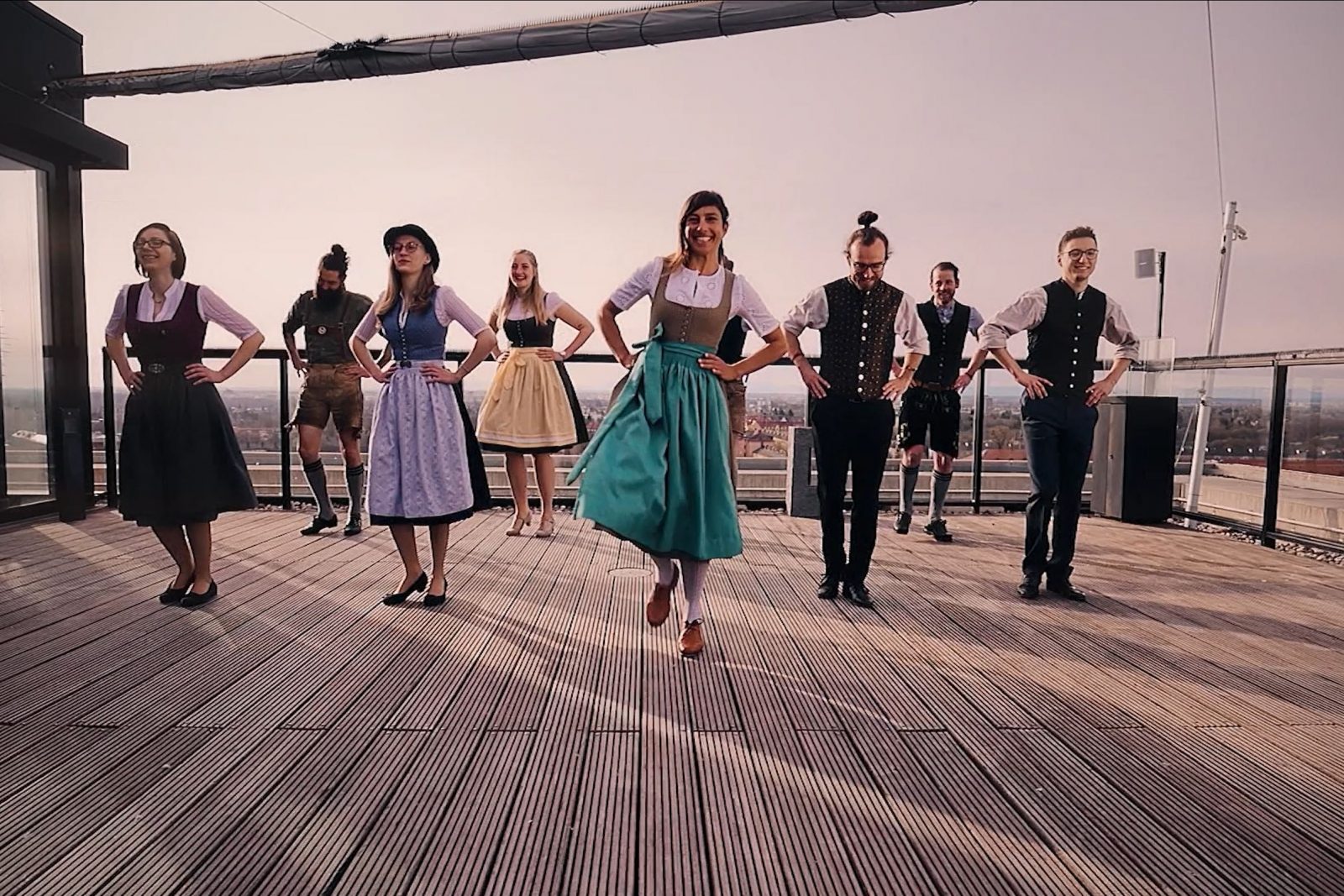 Eine Gruppe in bayerischer Tracht tanzt auf einer Dachterrasse.