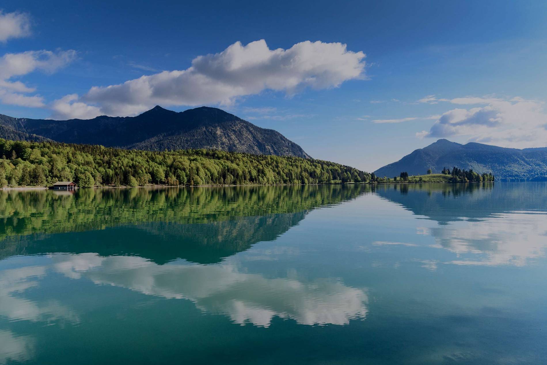 Blick auf den Walchensee bei schönstem Wetter, die Berge spiegeln sich im See.