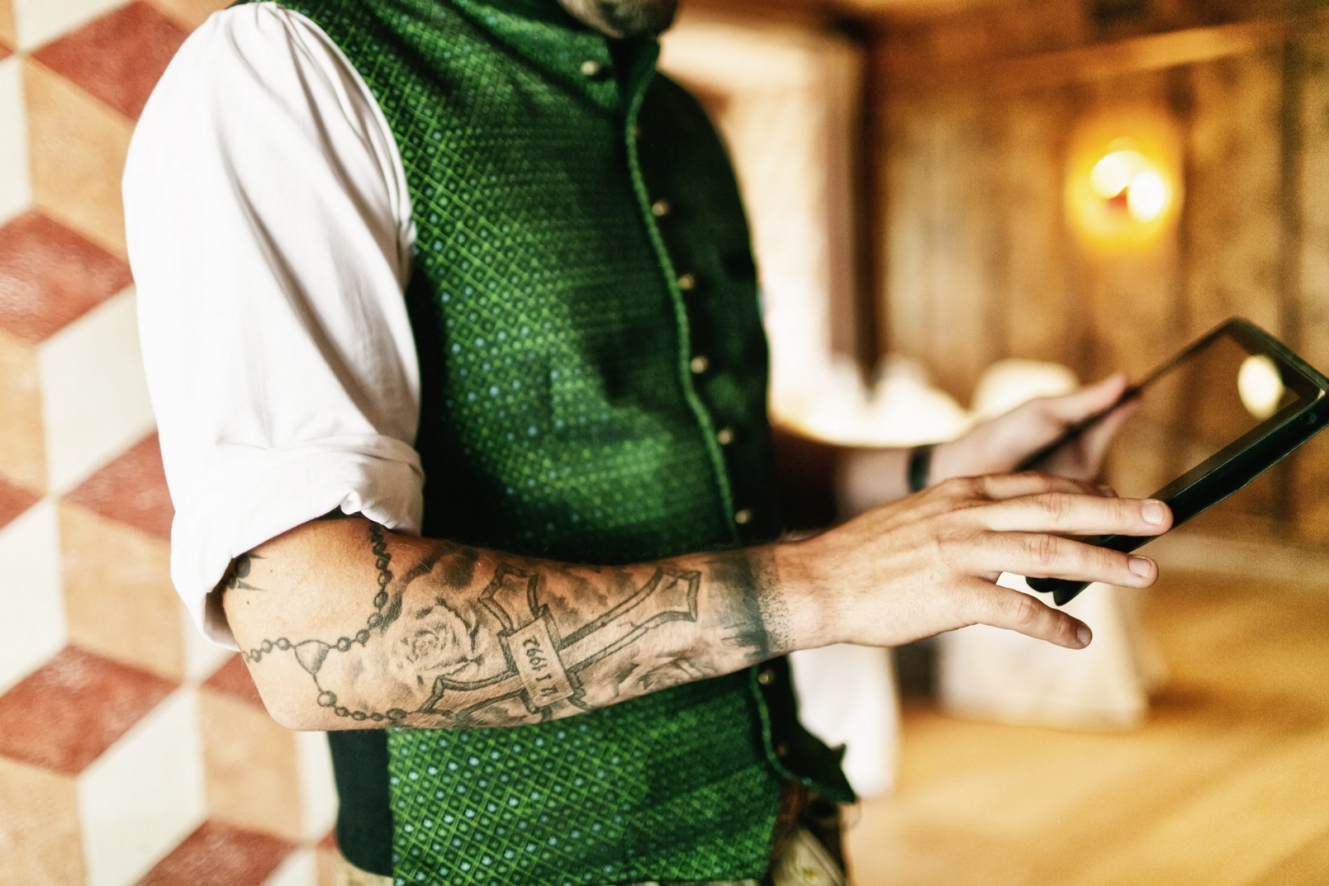 München, Platzl Hotel, MICE, Shooting Sommer 2021 Ein in Tracht gekleideter Mann mit tätowiertem Arm bedient ein Tablet.