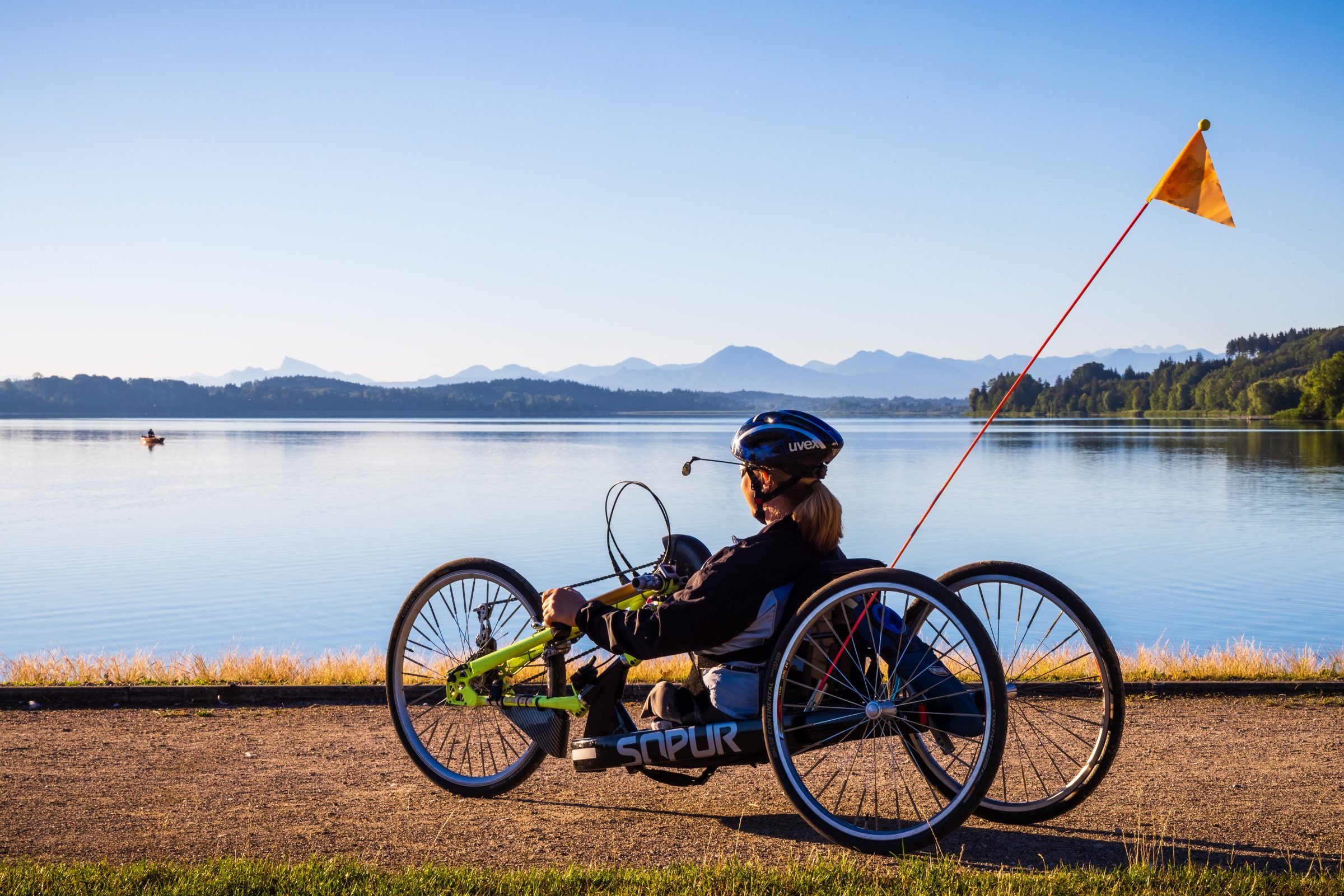 Eine Handbikefahrerin steht mit ihrem Bike bei bestem Wetter vor dem Chiemsee.