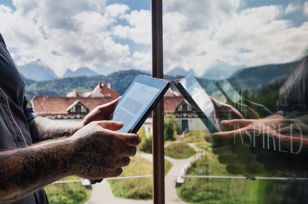 Ein Mann hält ein Tablet in der Hand. Er steht vor einer Scheibe, in der man die Spiegelung sieht.