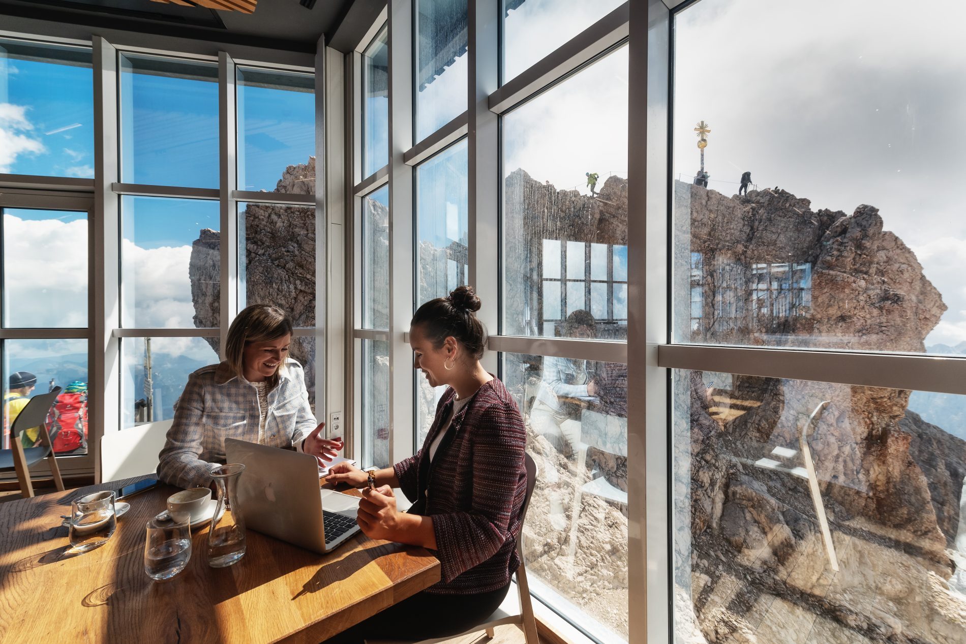 Deutschland, Bayern, Oberbayern, Zugspitze, MICE Zwei Geschäftsfrauen bei einem Meeting, im Hintergrund ist durch eine Glasscheibe die Zugspitze zu sehen.