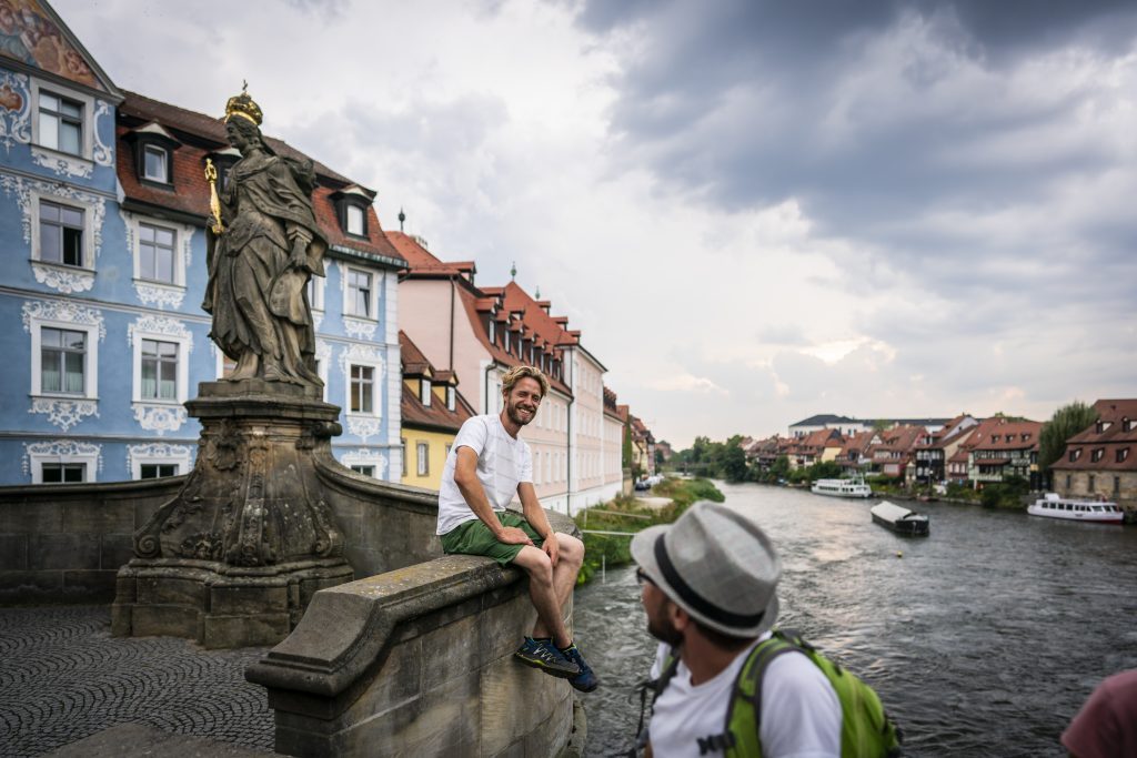 Bayern-Botschafter Sebastian Niedermaier sitzt auf einer Mauer am Fluss,