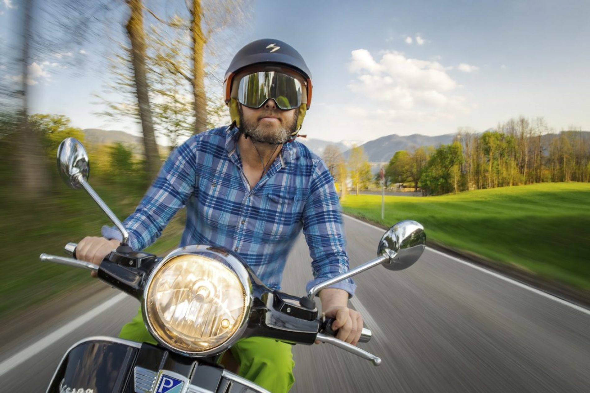 Dietmar_Denger Mann mit Motorradhelm und Visier fährt auf einer Landstraße; grüne Felder und Berge im Hintergrund.