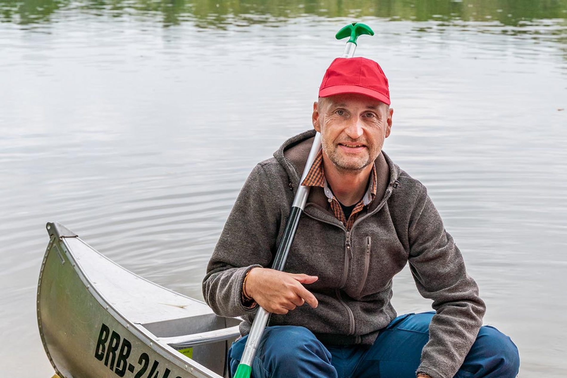 Autor Oliver Gerhard beim Paddelnauf einem Seitenarm der Havel, Ketzin/Havel, Havelland, Brandenburg, Deutschland Autor Oliver Gerhard im Aluminiumkanu am Ufer der Havel bei Ketzin/Havelland, Brandenburg; roter Hut, grüne Paddel.