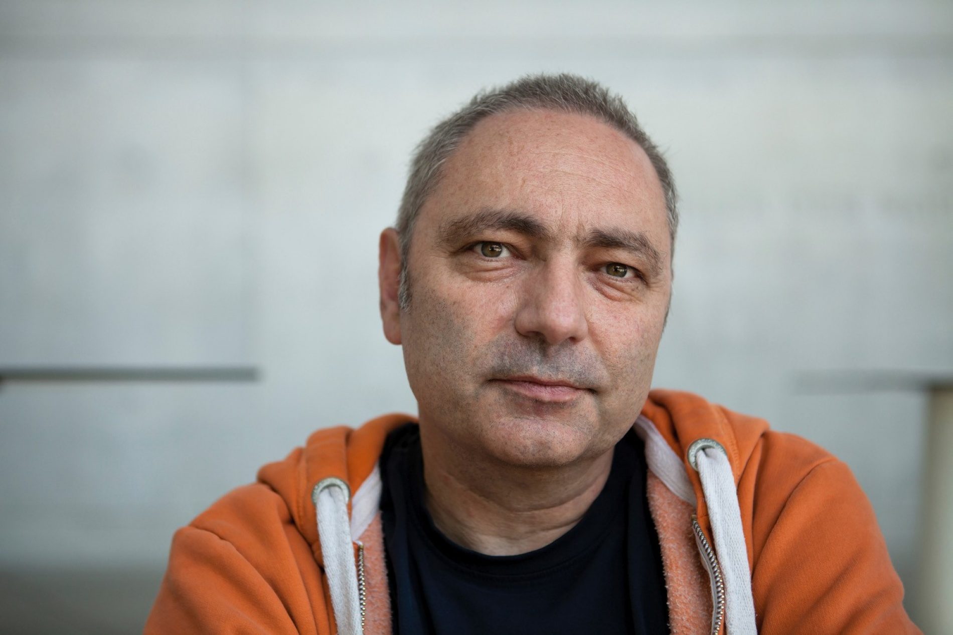 peter-von-felbert_2 Porträt eines Mannes mittleren Alters in orange Hoodie, neutrale Mimik, unscharfer Hintergrund