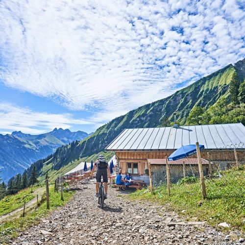 Ein Radfahrer fährt auf einem Schotterweg zu einer bewirtschafteten Hütte in den Oberstdorfer Bergen.