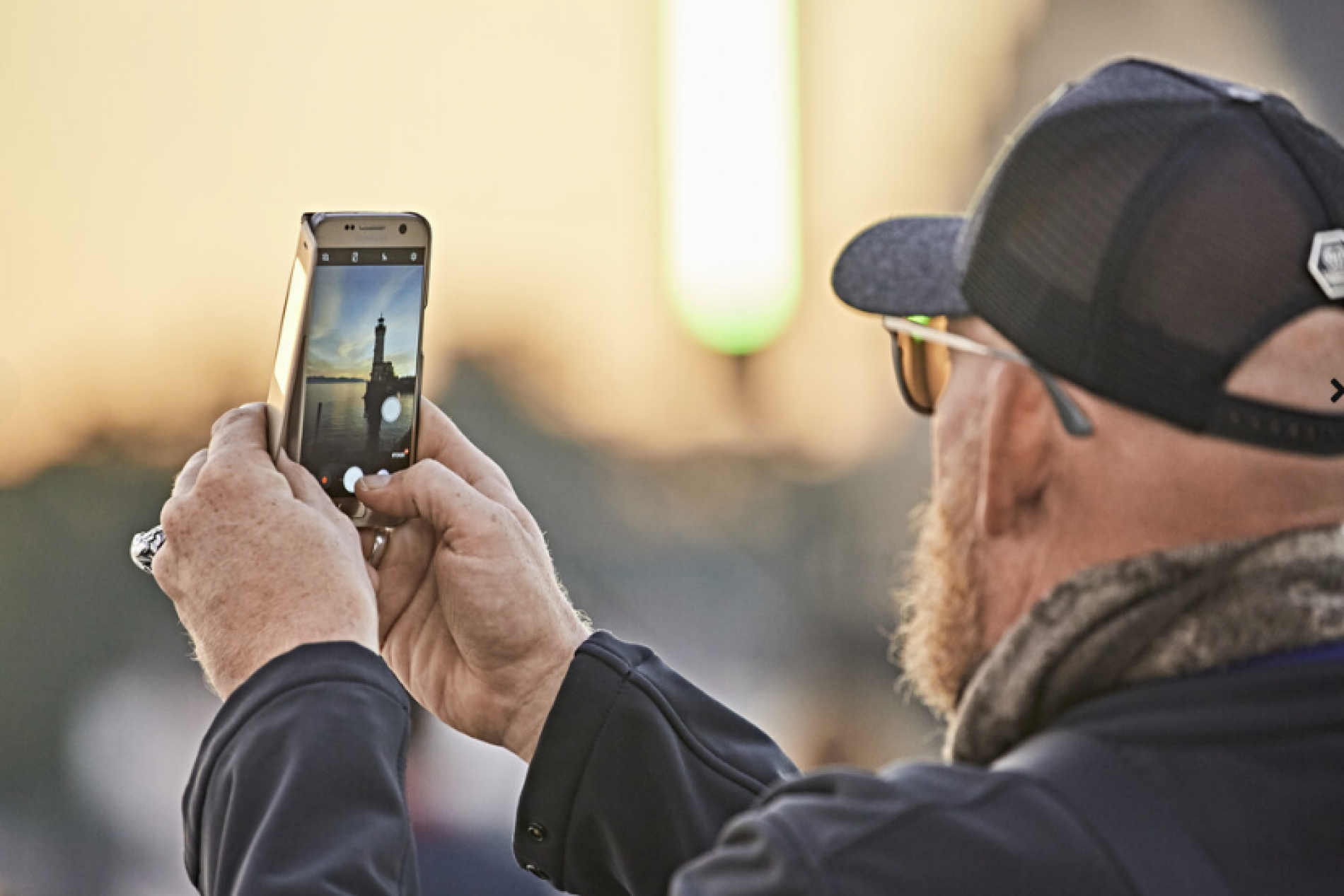 Person mit Kappe filmt ein Wahrzeichen mit dem Smartphone; unscharfer Hintergrund, Social-Media-Kontext.