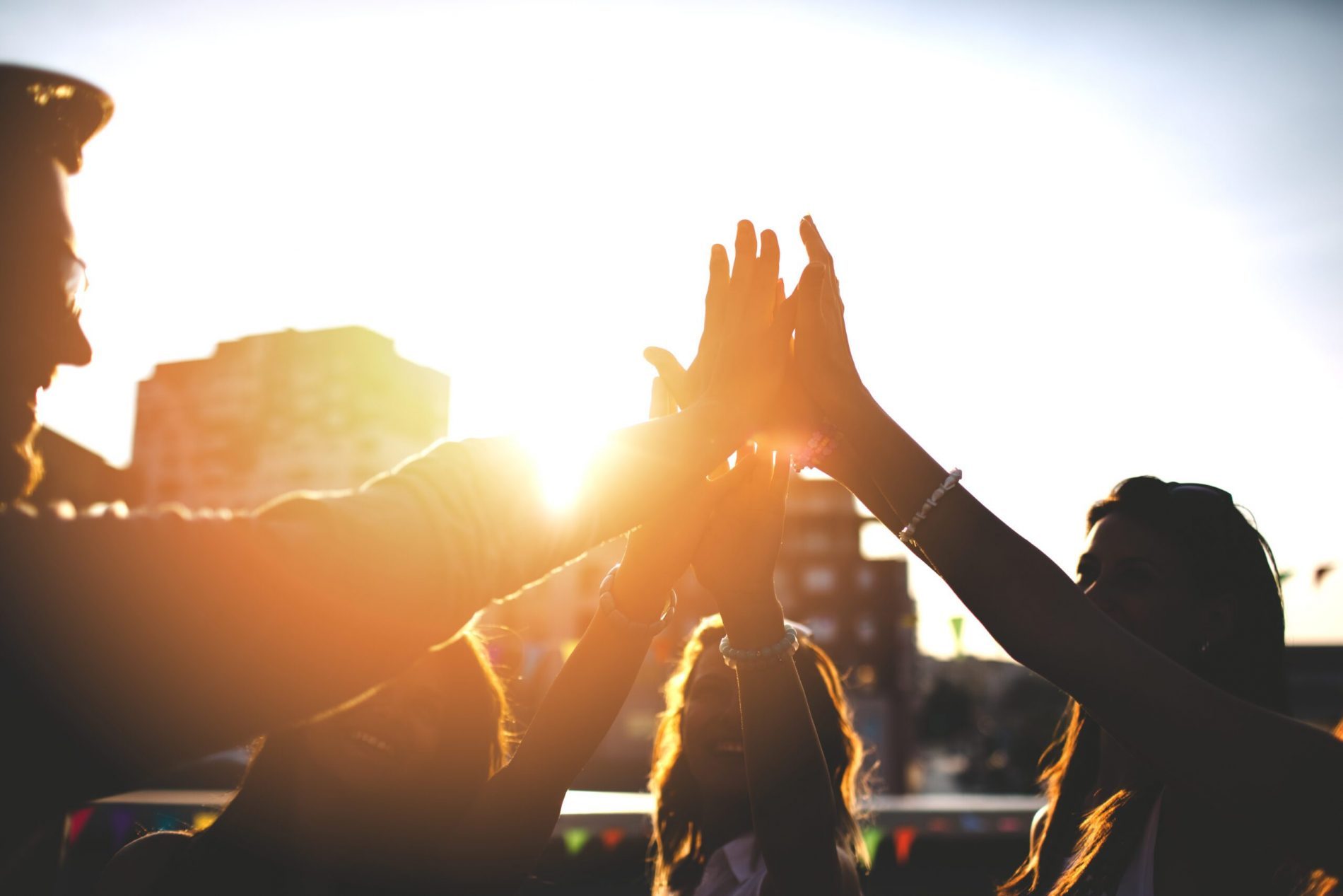 Happy friends at the rooftop doing high five Gruppe junger Menschen auf einer Dachterrasse gibt sich High Five bei Sonnenlicht, Teamwork