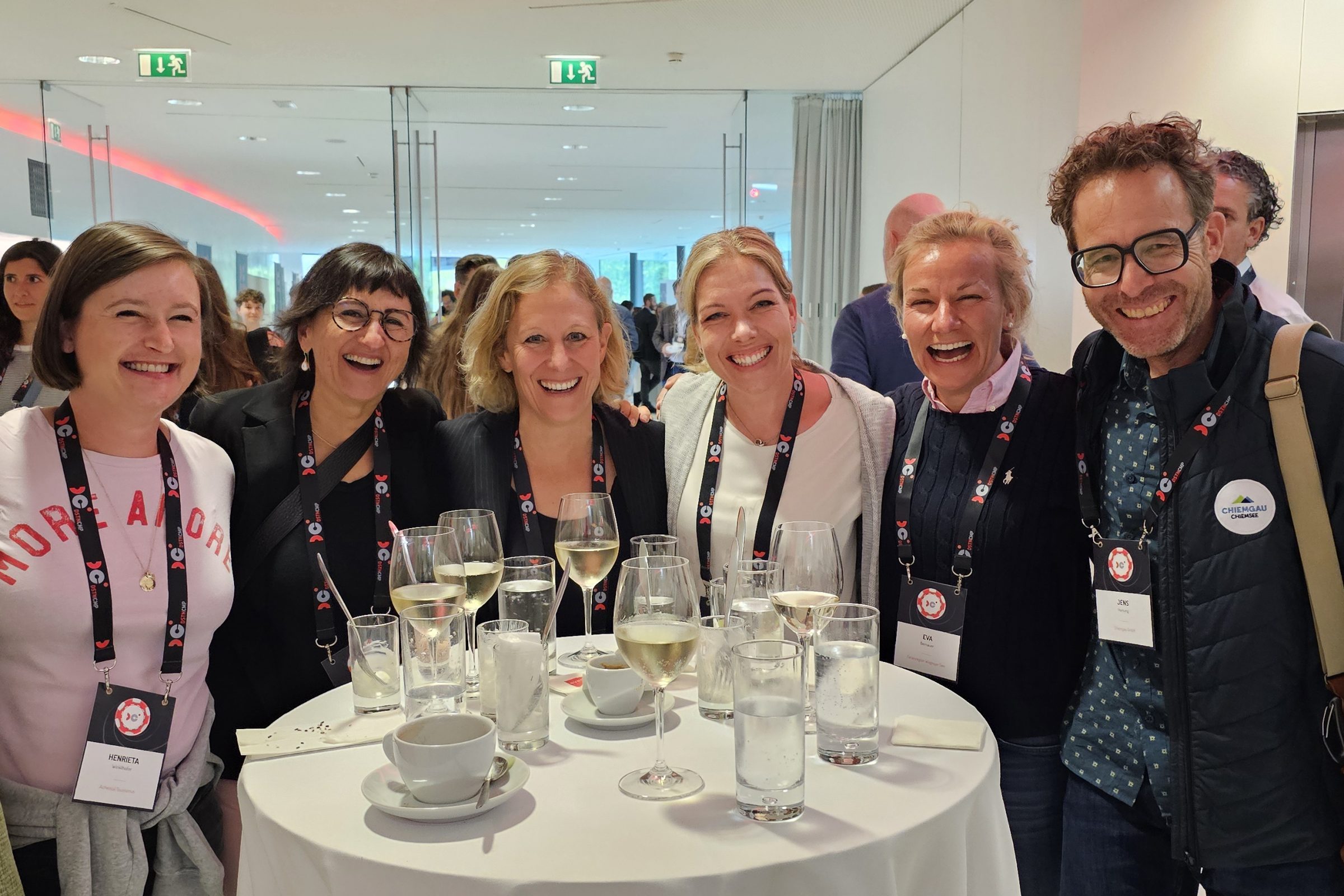 Gruppenfoto von sieben Teilnehmenden des Destination Camp 2024 beim Networking: Stehtisch, Gl&auml;ser Wein, Namensschilder, fr&ouml;hliche Atmosph&auml;re.