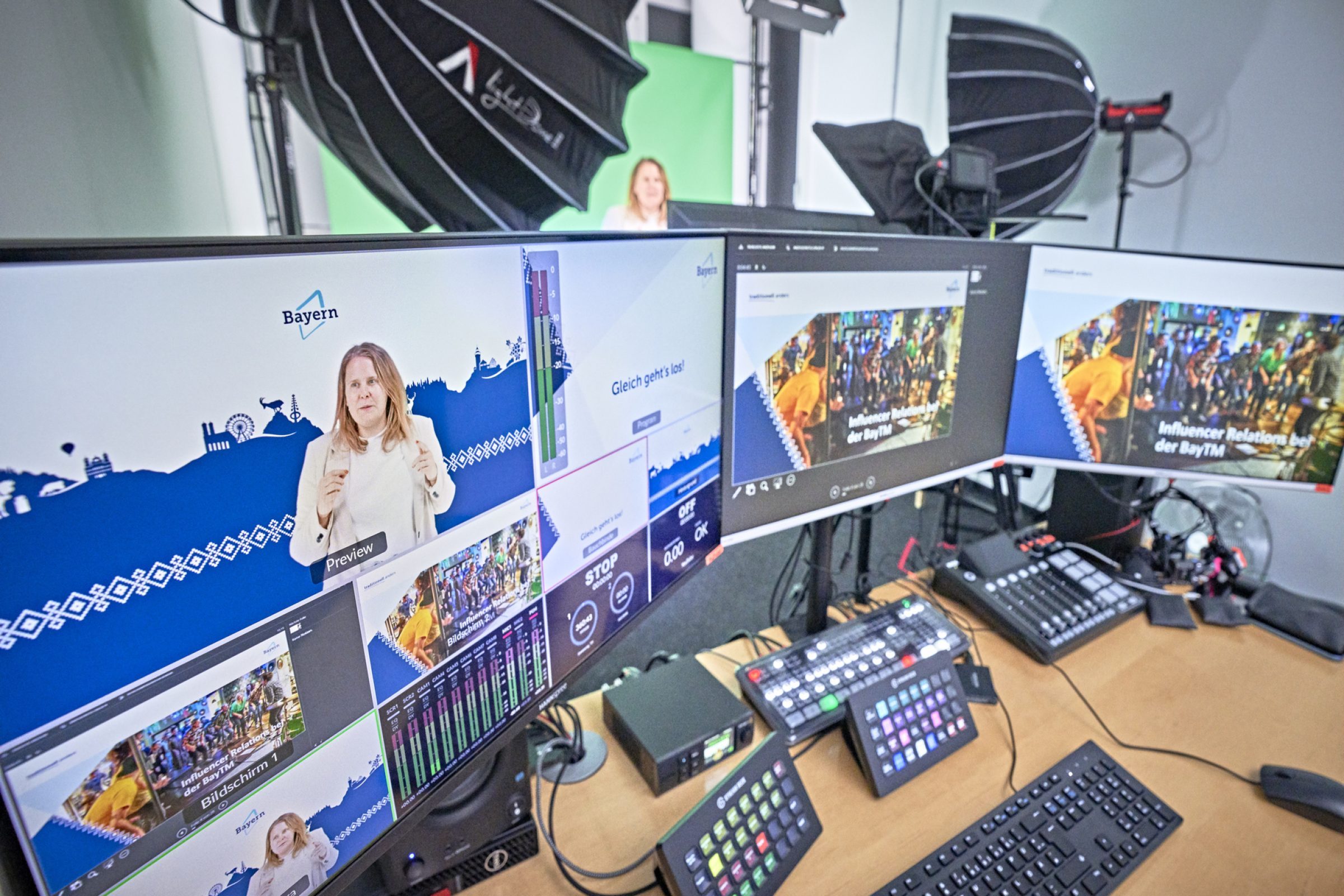 Studio-Setup f&uuml;r BayTM Marketing: Frau vor gr&uuml;nem Hintergrund, mehrere Monitore mit Bayern-Branding, Studiolicht und Technik.