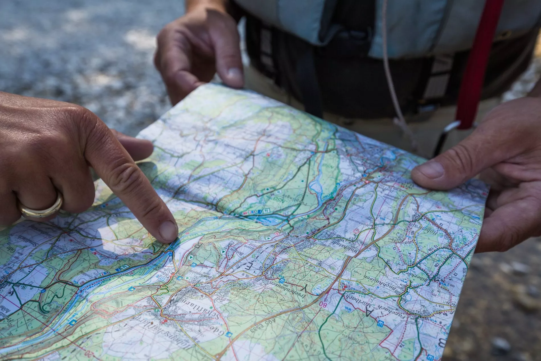 Zwei H&auml;nde halten eine detaillierte Karte, einer zeigt auf eine Route, im Hintergrund flie&szlig;t die Isar.