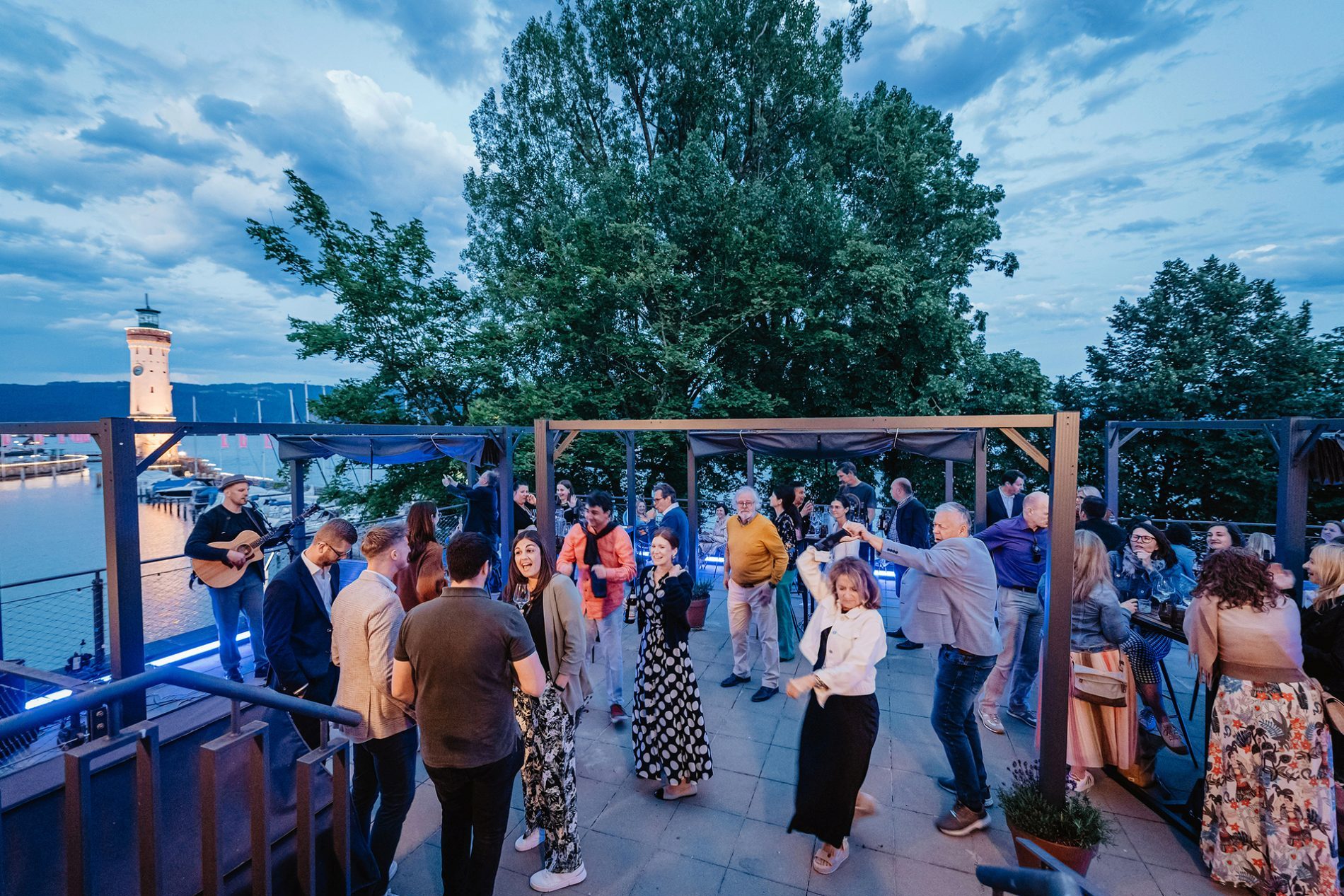 Deutschland, Bayern, Allgäu, Lindau, Bavaria Workshop 2024 Teilnehmer beim Bavaria Workshop: Outdoor-Event am Lindauer Hafen, Musik, Gespräche, Abendstimmung.