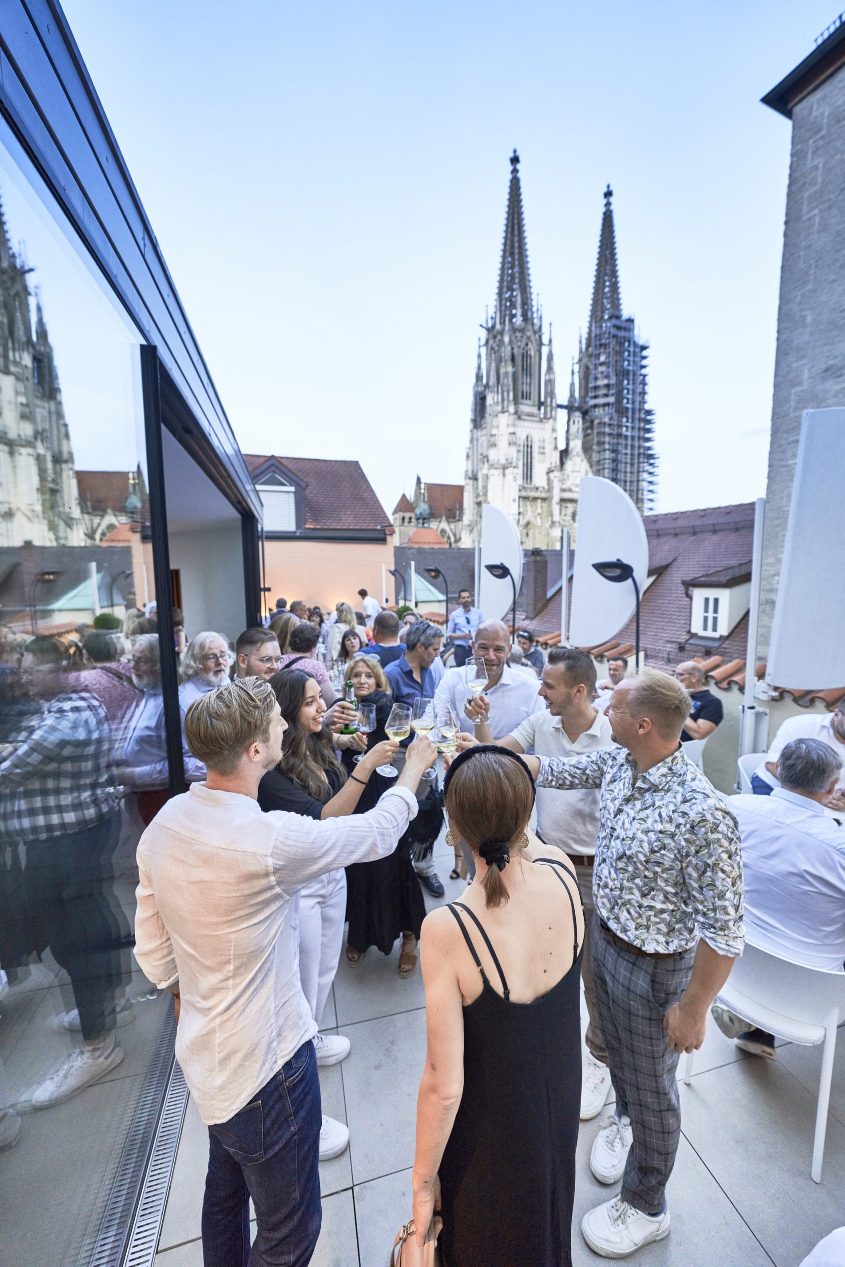 Bavaria Workshop Abend in Regensburg auf Dachterrasse Storstad; G&auml;ste sto&szlig;en mit Wein an, Kathedrale im Hintergrund.