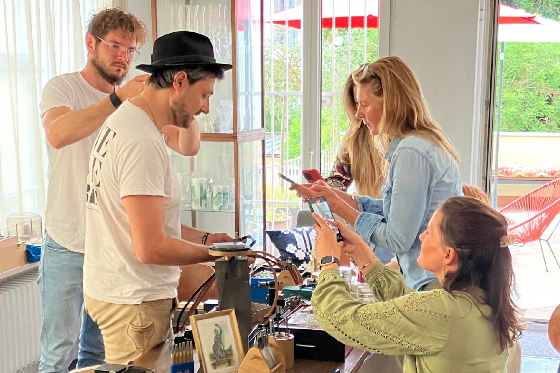 Mehrere Personen stehen und sitzen an einem Tisch und machen Fotos von den darauf ausgelegten Materialien.