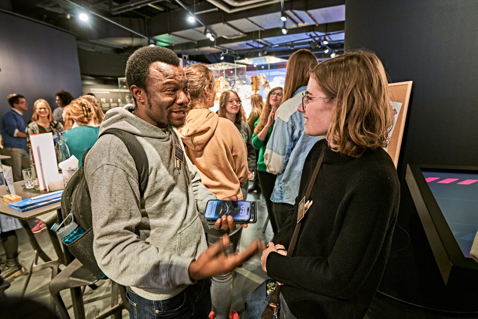 Zwei Besucher im Gespräch auf der Tourism Next Veranstaltung in der Allianz Arena; im Hintergrund weitere Gäste und Messestände.