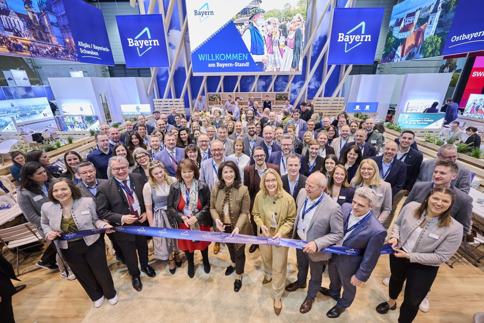 Gruppe von Messebesuchern vor dem Bayern-Stand bei ITB 2025, Banner und Ausstellungsfläche im Hintergrund.
