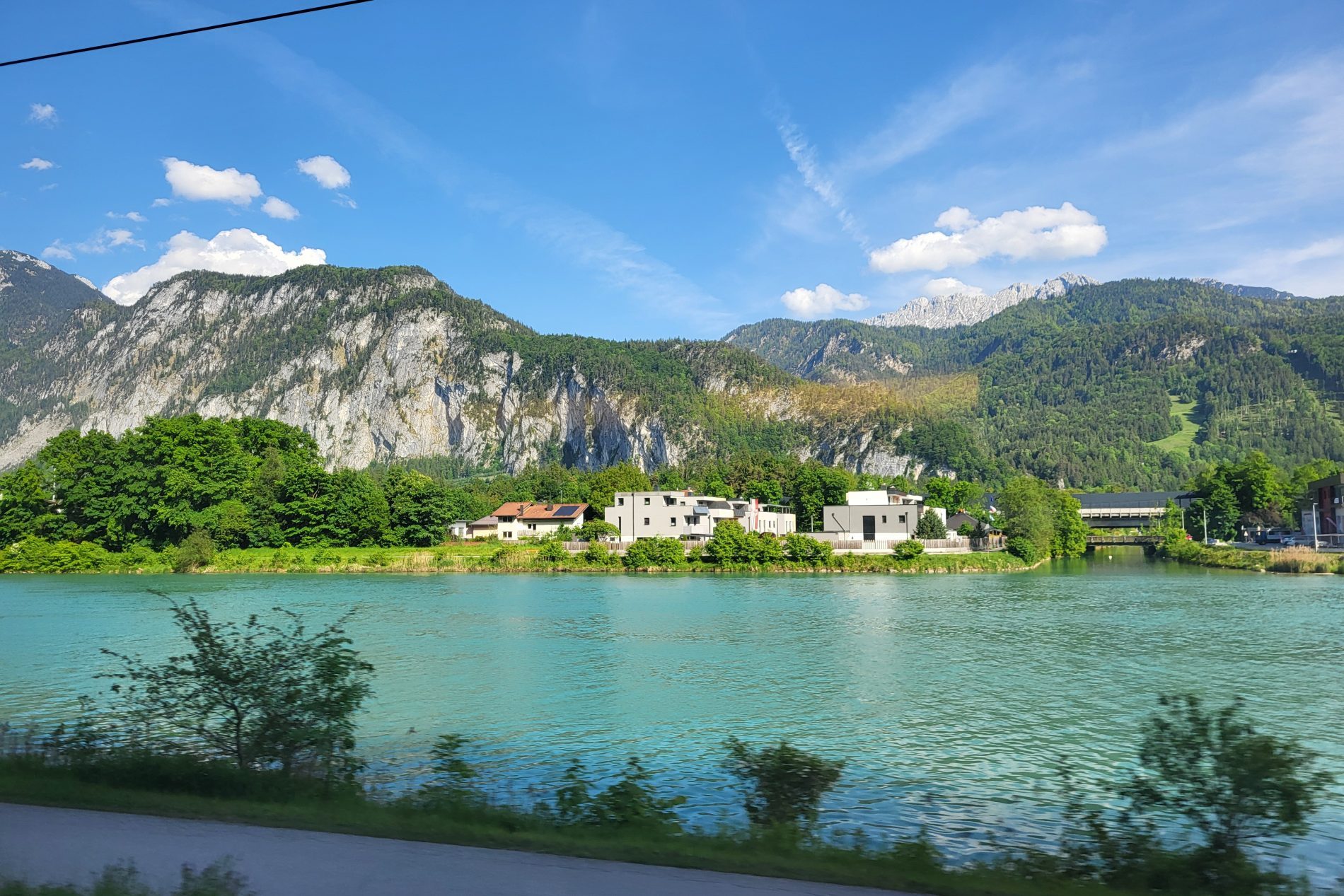 Rückfahrt: Flussufer mit türkisfarbenem Wasser, grüne Berge, Wohnhäuser am Ufer, blauer Himmel