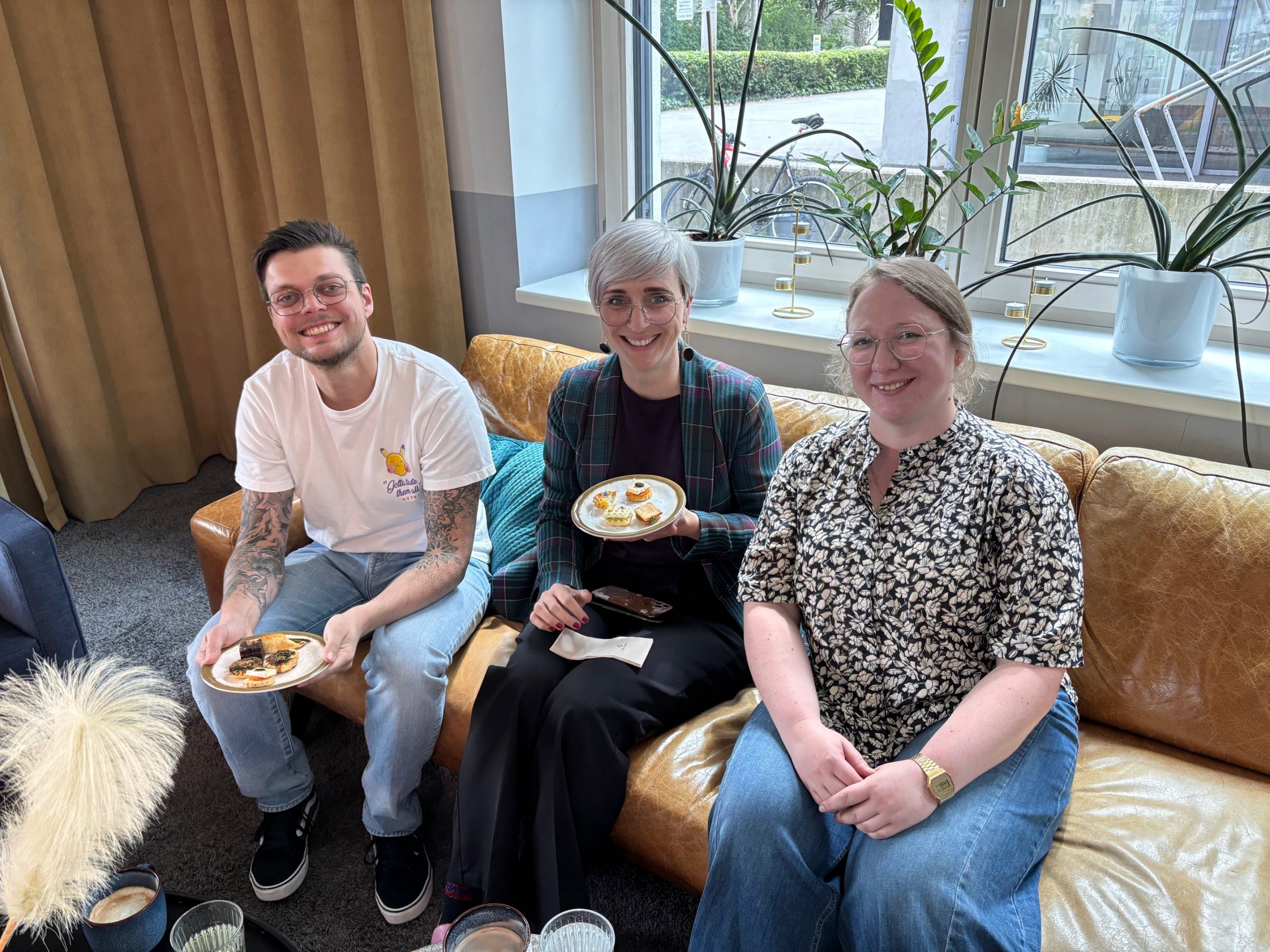 Drei Personen sitzen auf einem Ledersofa w&auml;hrend einer Kaffeepause beim ODTA Treffen Innsbruck 2025, essen Geb&auml;ck.