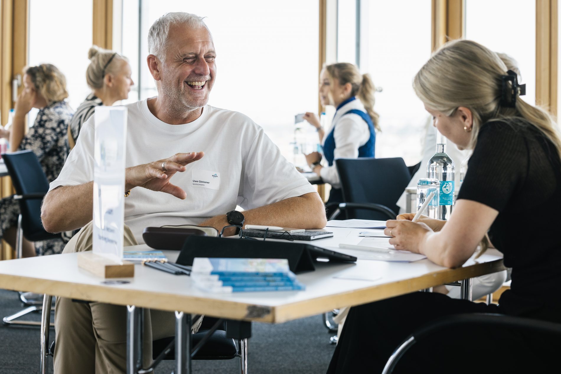 Meet Bayern Workshop 2025: Mann mit Namensschild spricht lächelnd mit Frau an Tisch; Hintergrund weitere Teilnehmer