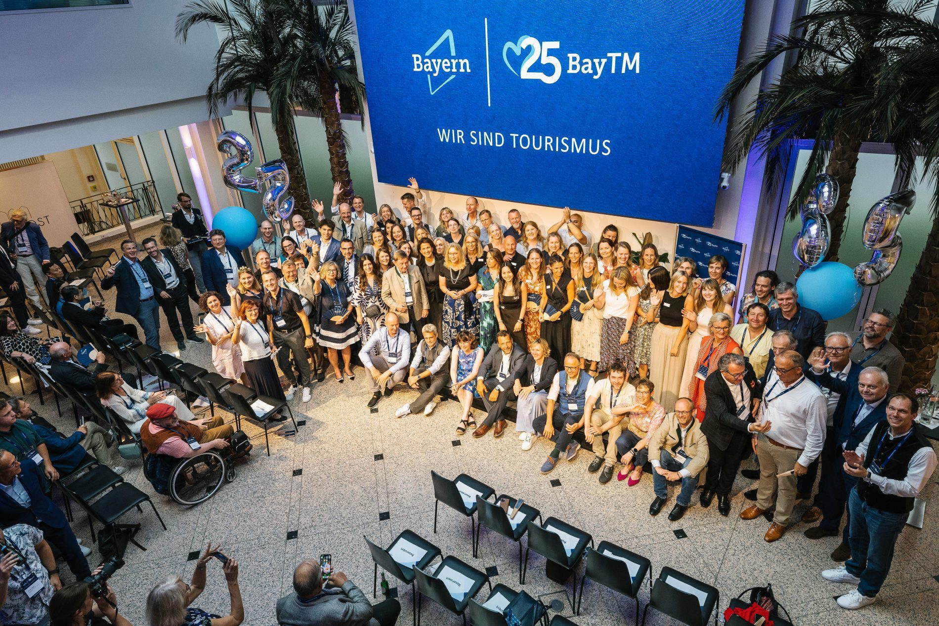Gruppe von Teilnehmern vor blauem BayTM Banner Bayern Connect 2025, 25 BayTM, Innenbereich der Veranstaltung, Ballons.