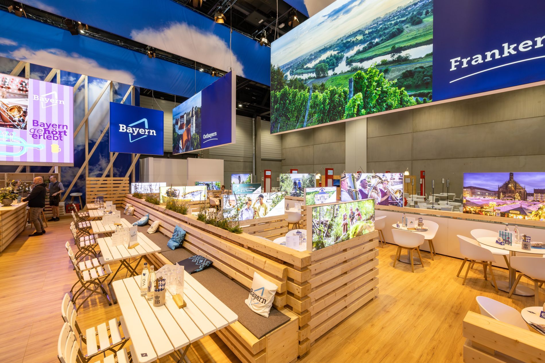 Bayern-Stand auf der ITB Berlin; Biergartentische zwischen Holzw&auml;nden, Gro&szlig;bildschirm mit Informationen, Banner mit Bayern-Logo.