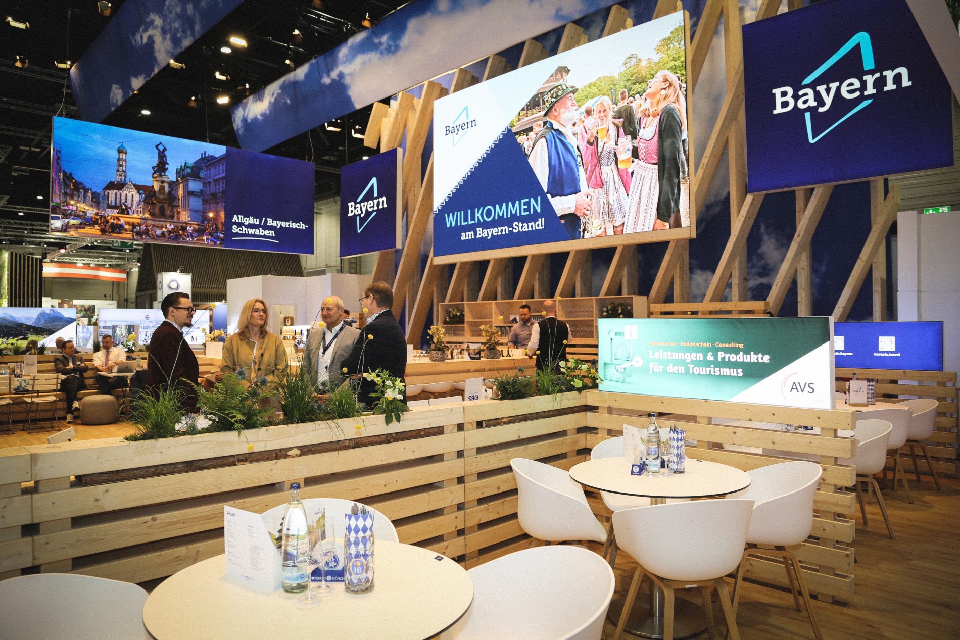 Bayern-Stand auf der ITB Berlin 2026: Holzrahmenkonstruktion, Banner, Gruppe von Menschen an einem 4er-Tisch.