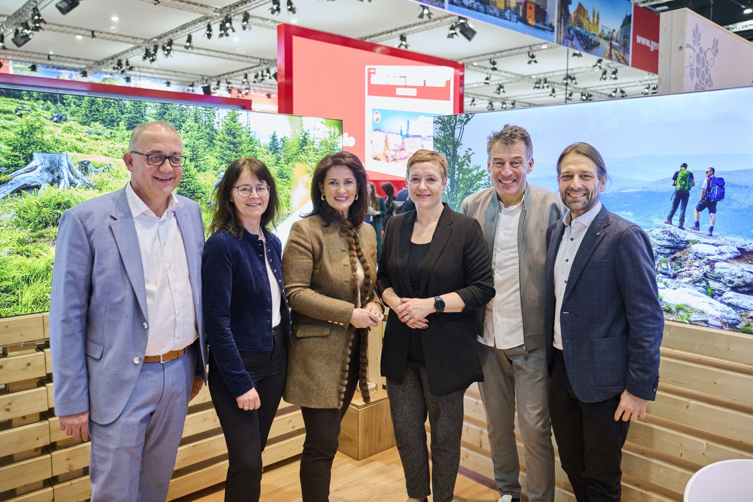 Sechs Personen am Bayern-Stand der ITB Berlin 2025 vor gro&szlig;en Landschaftstafeln, l&auml;chelnd und im Business-Look.