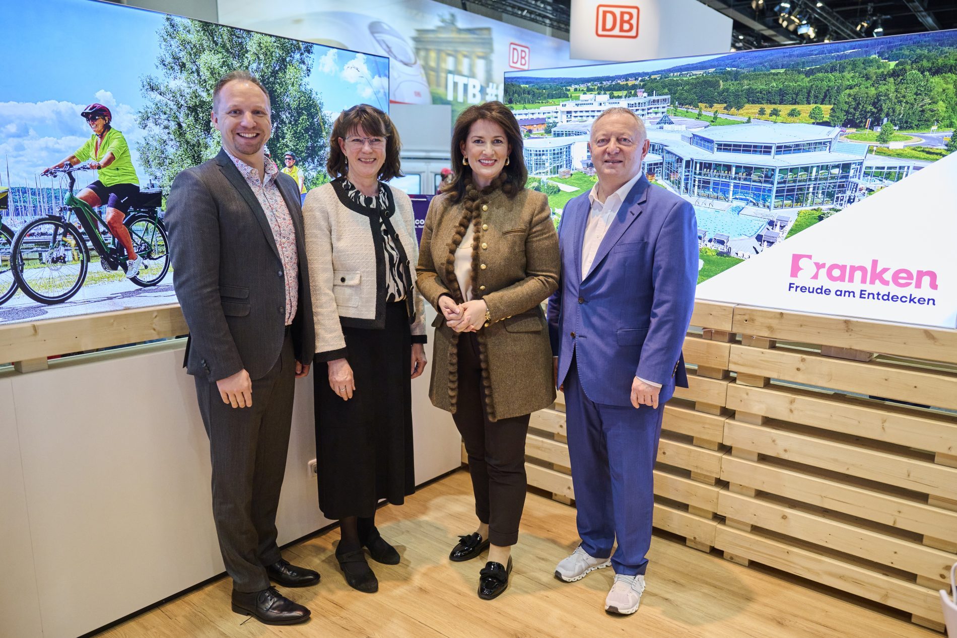 Vier Personen stehen am Bayern-Stand der ITB Berlin 2025, Hintergrund mit Großbild Fahrräder und Gebäudeanlage.