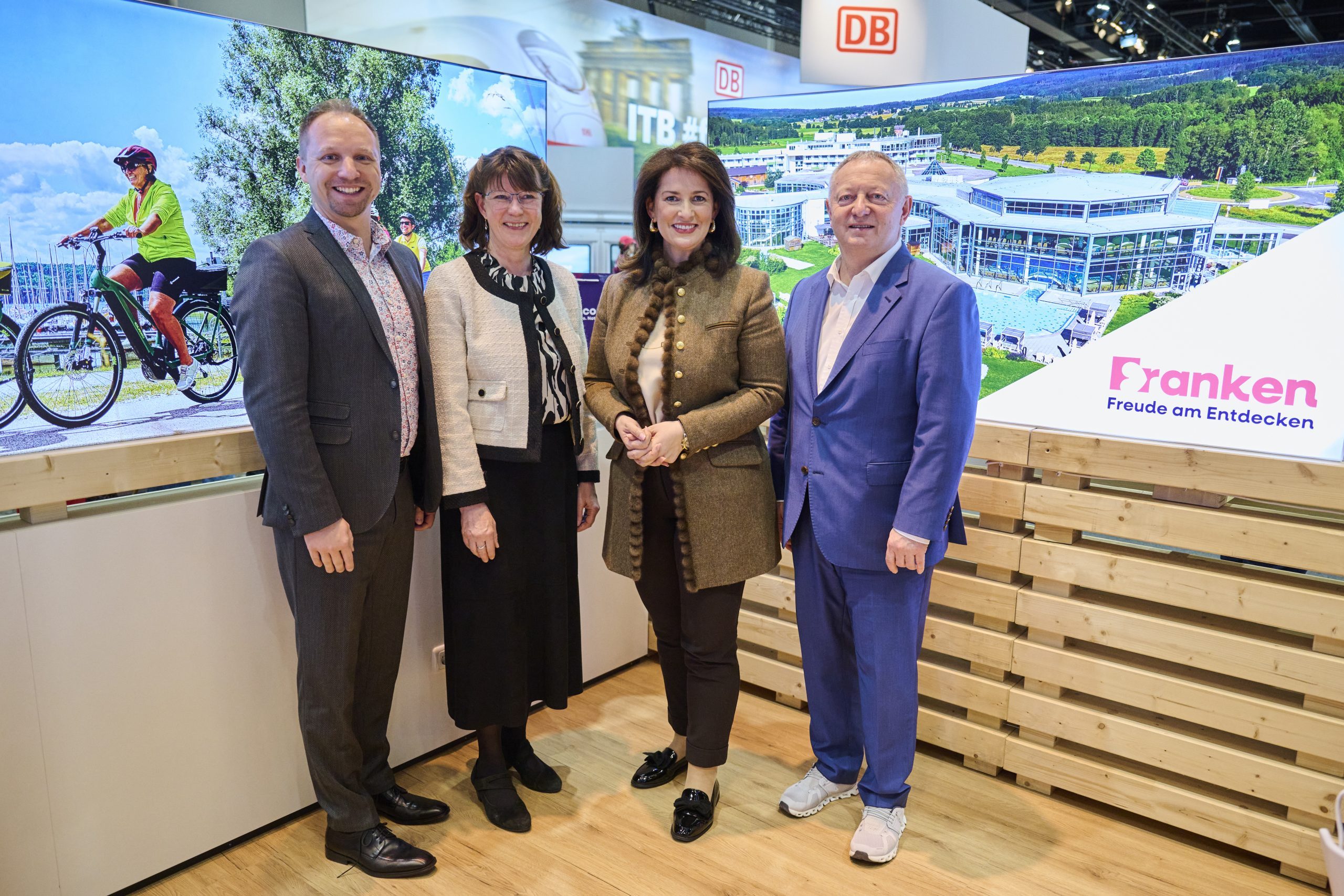 Vier Personen stehen am Bayern-Stand der ITB Berlin 2025, Hintergrund mit Gro&szlig;bild Fahrr&auml;der und Geb&auml;udeanlage.
