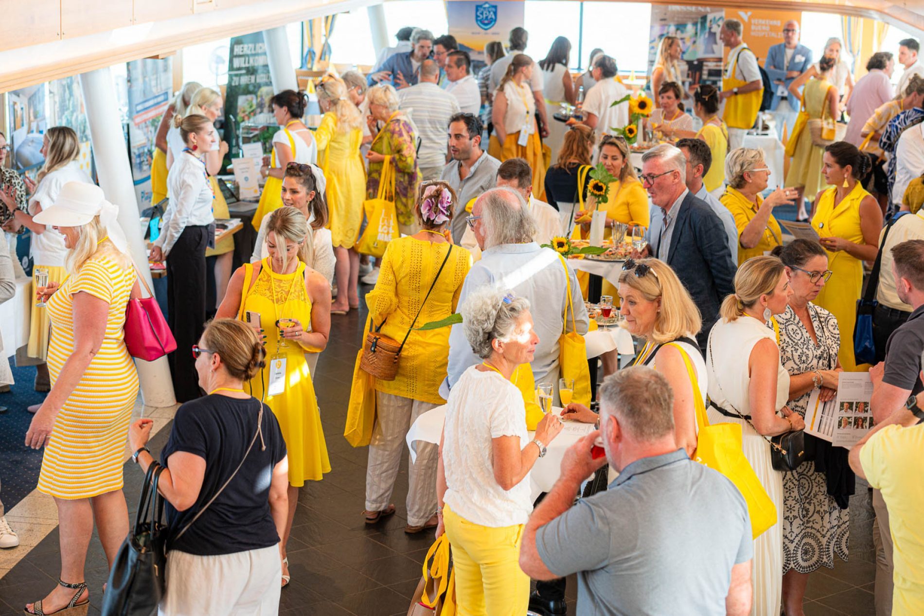 Menschenmenge beim MICE Branchentreff Starnberger See; viele Teilnehmende in gelb stehen, diskutieren und nehmen an Info-St&auml;nden teil.