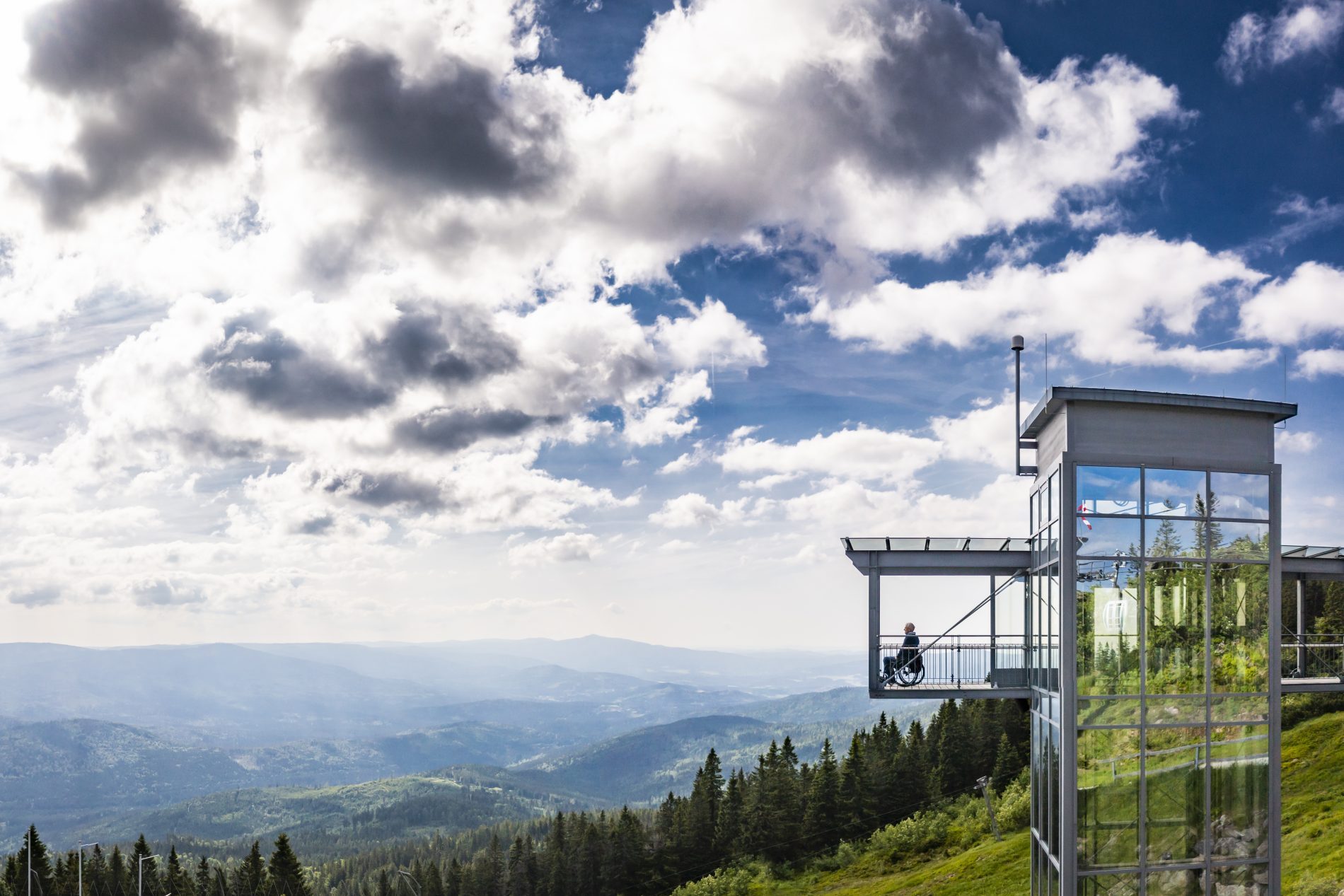 Gläserne Aussichtplattform am Arberland mit Blick über Wald- und Berglandschaft; eine Person steht am Geländer und genießt die Aussicht.