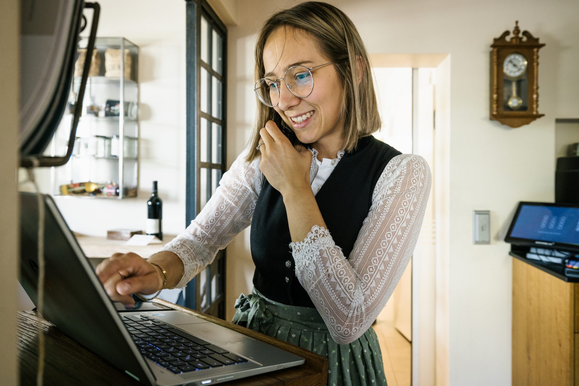 Frau mit Brille telefoniert am Laptop im Gasthaus Goldener Stern; Wanduhr hängt an der Wand.