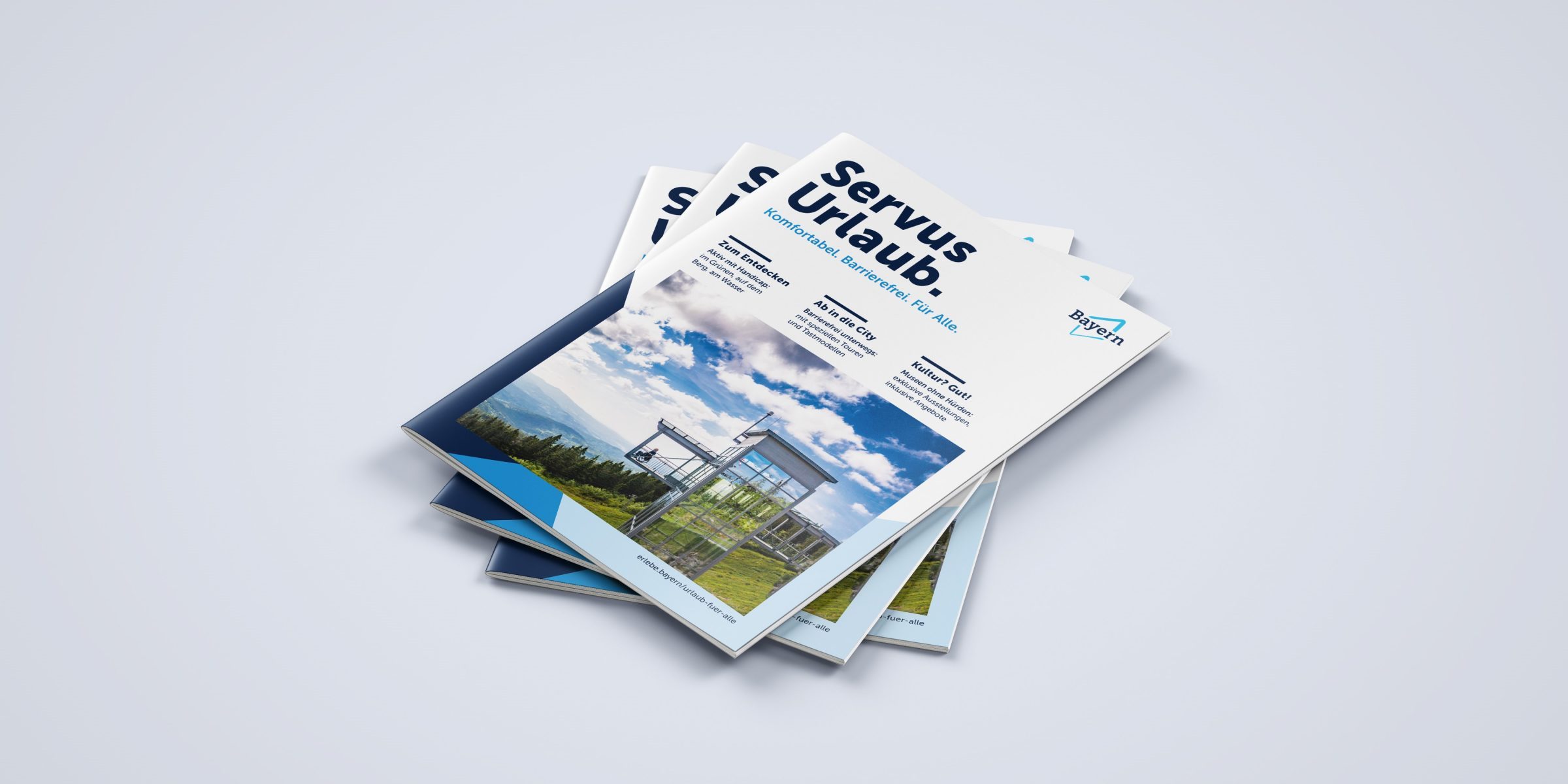 Mehrere Prospekte mit dem Titel Servus Urlaub Bayern Barrierefrei Quer stapeln sich auf hellem Hintergrund, Kontext Kooperationsm&ouml;glichkeiten.