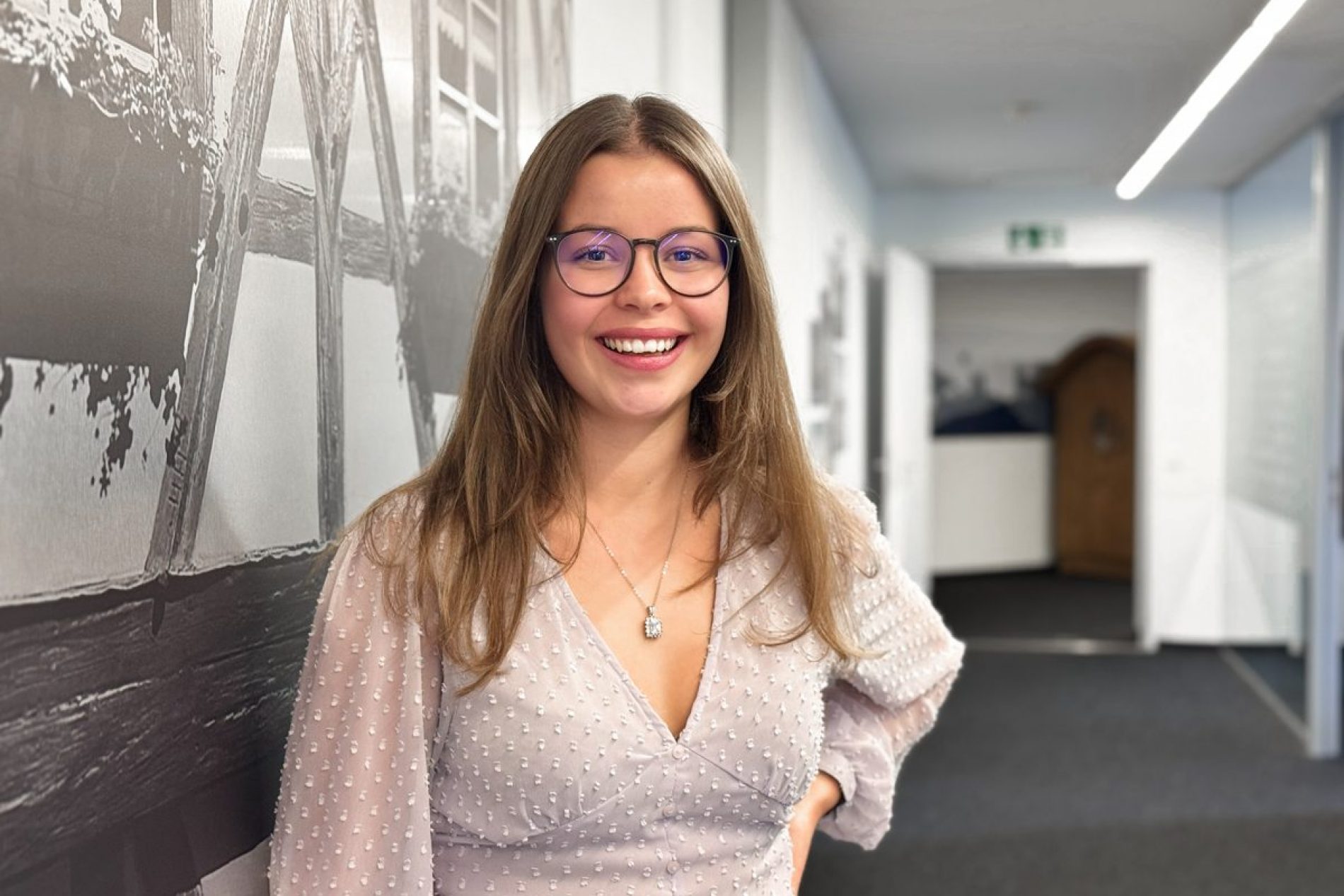Portrait einer freundlichen Frau mit Brille in einem hellen Flur, rosa Bluse mit Muster.