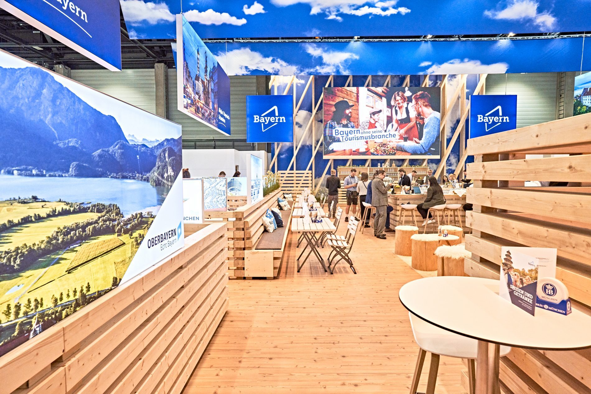 Bayern-Stand auf der ITB 2024 mit Holzbalken, Bayern-Logos, Besuchende am Barbereich.