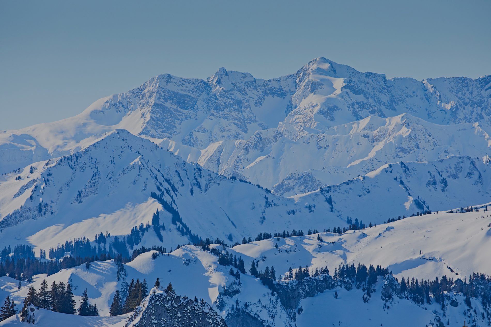 __W5A9849 (c) erlebe.bayern – Gert Krautbauer Schneebedeckte Berglandschaft mit hohen Gipfeln, vorderem Wald aus Nadelbäumen und klarem blauen Himmel.