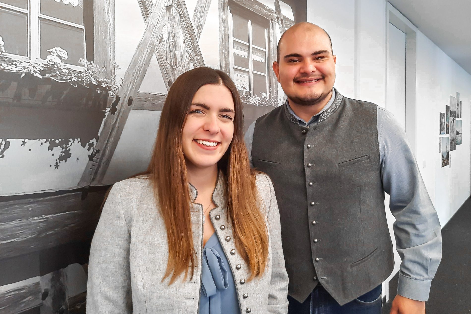 Zwei Personen in grauen Blazern posieren im Flur; Wandtext im Hintergrund, Kontext Kooperationsm&ouml;glichkeiten.