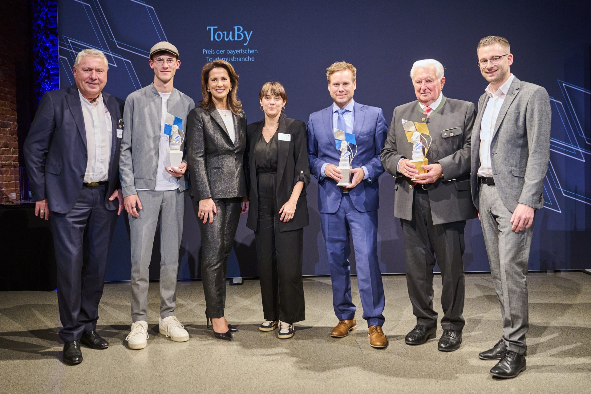 Gruppenfoto von sieben Personen bei der TouBy-Verleihung in Bayern. Drei Personen halten Auszeichnungen in den H&auml;nden.