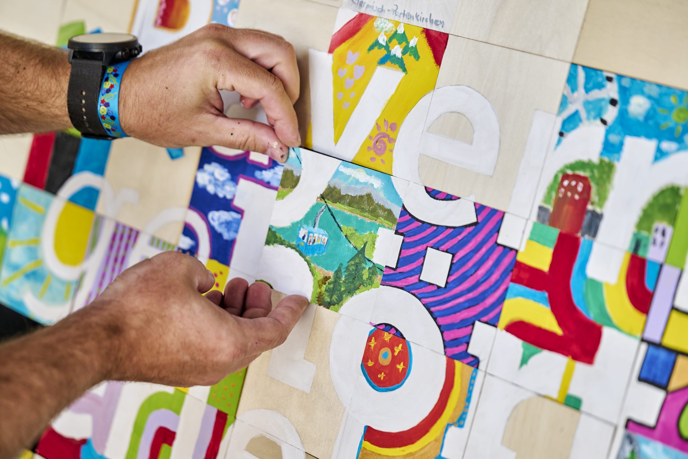 H&auml;nde setzen ein buntes Puzzlest&uuml;ck mit Landschaftsmotiv in ein kreatives Kunstwerk beim B2B-Tourismusfestival.