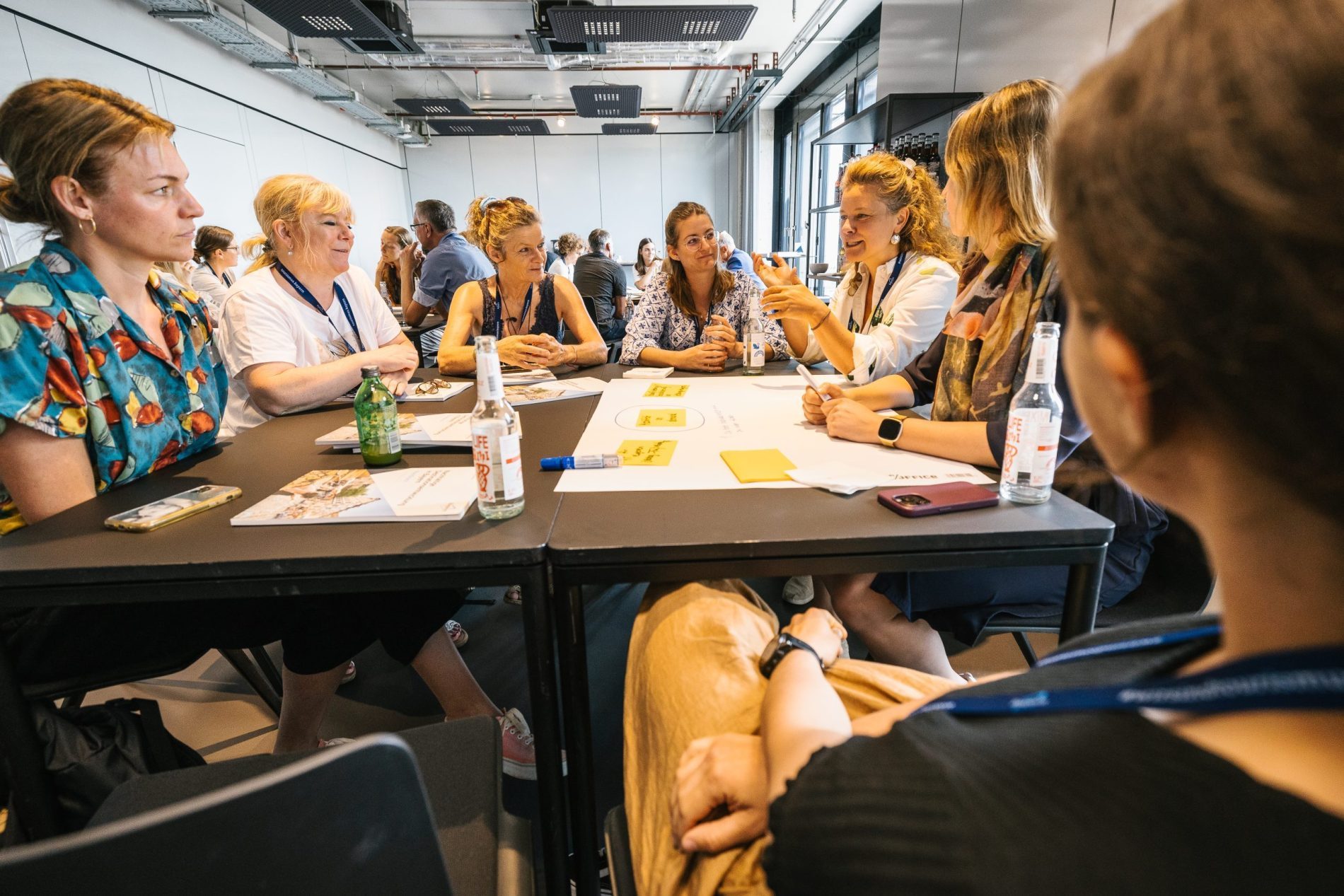 Eine Gruppe von Personen sitzt in Workshopatmosph&auml;re an einem Schreibtisch und diskutiert.